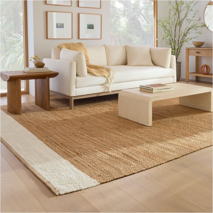 Jute rugs placed in a living room , having white sofas and table in it.